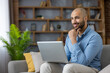 © Liubomir - Smiling young man relaxing on a sofa while telecommuting with his laptop, focused and confident remote worker studying or freelancing from a comfortable modern home office