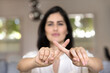 © fizkes - Young Latin woman showing index fingers crossed in ban, prohibition, stop gesture, expressing disagreement, protest against violence, bulling, discrimination, abuse