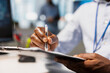 © DC Studio - Close up of office worker writing on clipboard while seated at desk, doing accounting tasks. Employee in modern workplace completing paperwork during routine administrative tasks