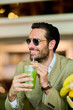 © Teodor Lazarev - Stylish man in sunglasses enjoying a refreshing green detox juice, smiling while embracing healthy living and a smart casual lifestyle