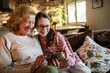 © Geber86 - Smiling grandmother and granddaughter using smartphone on sofa at home