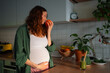 © wifesun - Pregnant woman enjoying the scent of a fresh orange, standing in her kitchen with a green smoothie on the counter, focusing on healthy eating and prenatal nutrition