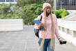 © wavebreak3 - Adult African American woman wearing pink hoodie and beanie holding folders and phone on walkway