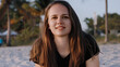 © 4kclips - Wellness tourism and a beach getaway A smiling young woman with long brunette hair is shown in a close-up portrait enjoying a tropical vacation on a sandy beach at sunset. The scene promotes travel re