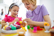 © sofiko14 - A mother and her daughter are happily painting colorful Easter eggs together at a wooden table, creating festive decorations for the holiday