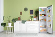 © Pixel-Shot - Open fridge full of different fresh products with flowers and utensils on counter near green wall in kitchen