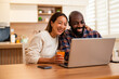 © djoronimo - Two partners laugh together while using a laptop at home, they have a video call.