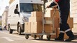© Tina - A delivery worker pushes a cart loaded with cardboard boxes on a city street. A delivery van is parked nearby, indicating a logistics operation.