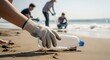 © RIDOY - Volunteer hand picking up plastic water bottle from the sand during a beach cleanup event to protect the marine ecosystem and reduce pollution