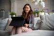 © Parichat - Asian woman smiling, using a digital tablet for remote work or online learning on a couch