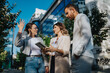 © qunica.com - Three professionals in business casual discuss ideas outdoors. They stand on a sunny city street, engaged in conversation with a tablet.