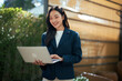 © Parichat - Young Asian businesswoman working on laptop outdoors smiling