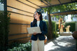 © Parichat - Young Asian professional woman holding laptop smiling outdoors