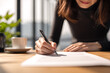 © EricMiguel - Close-up of a woman signing a contract at a wooden desk with coffee - professional document signing in modern office, business agreement and paperwork