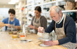 © JackF - Mature man at table molds cup from wet clay in a pottery workshop