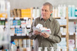 © JackF - Elderly man with different packages of pills and medicines in a European pharmacy. Pensioner came to the pharmacy for medicines with a prescription from a therapist