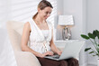 © New Africa - Woman using laptop in armchair at home