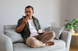 © ArvStd - An adult man is relaxing on a sofa inside the house, using a cellphone to communicate, making calls or talking on the cellphone with someone.