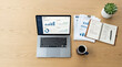© Anindito - Overhead view of a modern workspace with a laptop showing business analytics, financial documents, a notebook, and coffee on a wooden desk.