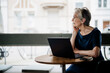 © Westend61 - Senior woman using laptop in a caf� looking out window happy and healthy