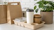 © Johnnii - Eco-friendly disposable cups, containers, and bags made from biodegradable materials are displayed alongside a green houseplant on a light wooden surface.