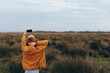 © SHOTPRIME STUDIO - A woman in a brown jacket and hat takes a selfie outdoors in a grassy field under a cloudy sky. Lifestyle concept focused on nature, freedom, and casual outdoor activity.