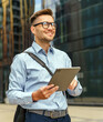 © muse studio - Smiling young professional walks confidently with a digital tablet in a modern urban environment