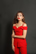 © artmim - Confident young woman in red suit standing against black studio wall background