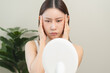 © Pormezz - An Asian young woman looking at the mirror and feeling worried about her facial skin problem that cracked and aging.