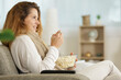 © auremar - woman sitting on sofa eating popcorn beside remote at home