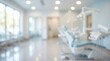 © Nest - A bright, blurred view of a modern dentist's office features a light blue dental chair and various medical equipment, suggesting a clean and welcoming healthcare environment.