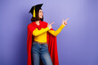 © deagreez - Young graduate in cap and cape with yellow top jeans and glasses smiles and points both sides against purple background in a cheerful stylish scene