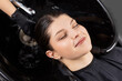 © Parilov - Young happy caucasian woman enjoying relaxing hair wash at salon black sink, top view