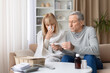 © Anastasiya - Senior couple at home checking thermometer while woman is sick and coughing. Mature man helping ill partner during cold or flu illness, representing domestic healthcare and family support