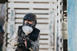 © qunica.com - Masked operative in tactical gear aims a paintball gun in an industrial warehouse. A training or simulation scene unfolds in a rugged backdrop.