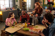 © Mediaphotos - Group of multiethnic young people sitting around table eating pizza and drinking beverages, smiling and talking, pizza boxes and snacks , casual indoor gathering, relaxed social interaction