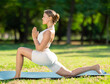 © JackF - Positive young yogini in white comfortable sportswear doing yoga on mat in green sunlit summer park, performing Anjaneyasana or Crescent Low Lunge Pose, demonstrating flexibility and balance
