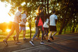 © Studio Romantic - Full-length view, group of young people running along scenic route in summer park during sunset. Men and women dressed in sportswear jogging outdoors. Sports, healthy and active lifestyle concept
