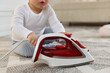 © New Africa - Child safety at home. Little boy playing with iron on floor indoors, closeup