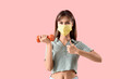 © Pixel-Shot - Young woman in medical mask with dumbbell showing thumb-up on pink background. Immunity concept