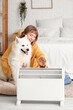 © Pixel-Shot - Young woman with cute dog warming near radiator in bedroom