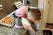 © Татьяна Швец - little boy pouring milk into stand mixer bowl while cooking pancake batter in kitchen, child helping prepare homemade breakfast dough with eggs and ingredients