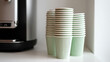 © photo for everything - Stack of fresh mint green disposable coffee cups next to an out-of-focus beverage machine, ready for use in a clean, modern setting