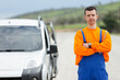 © Fatih - Confident professional mechanic in orange and blue uniform standing with crossed arms on the roadside for emergency car assistance.