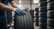 © Nusrat - Mechanic wearing blue gloves carefully inspecting car tire in auto service workshop with many tires stacked in background, professional automotive expert performing routine maintenance