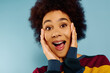 © LIGHTFIELD STUDIOS - Stylish woman with curly hair in colorful attire shows surprise against a blue background