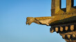 © AmazingAerialAgency - Aerial view of a weathered gargoyle perched on a stone structure, its aged surface contrasted against the clear blue sky, Saint-Pol-de-Leon, Brittany, France.