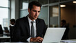 © P.W-PHOTO-FILMS - A man types intently on a laptop in a modern office. He wears a suit and tie.