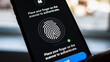 © P.W-PHOTO-FILMS - A smartphone displays fingerprint scanning instructions. A finger touches the scanner, initiating authentication.