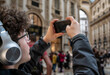 © Massimo Parisi - Milan, italy, april 1, 2024. Young man wearing headphones and glasses taking vertical smartphone video or picture of classical architecture inside famous milan gallery